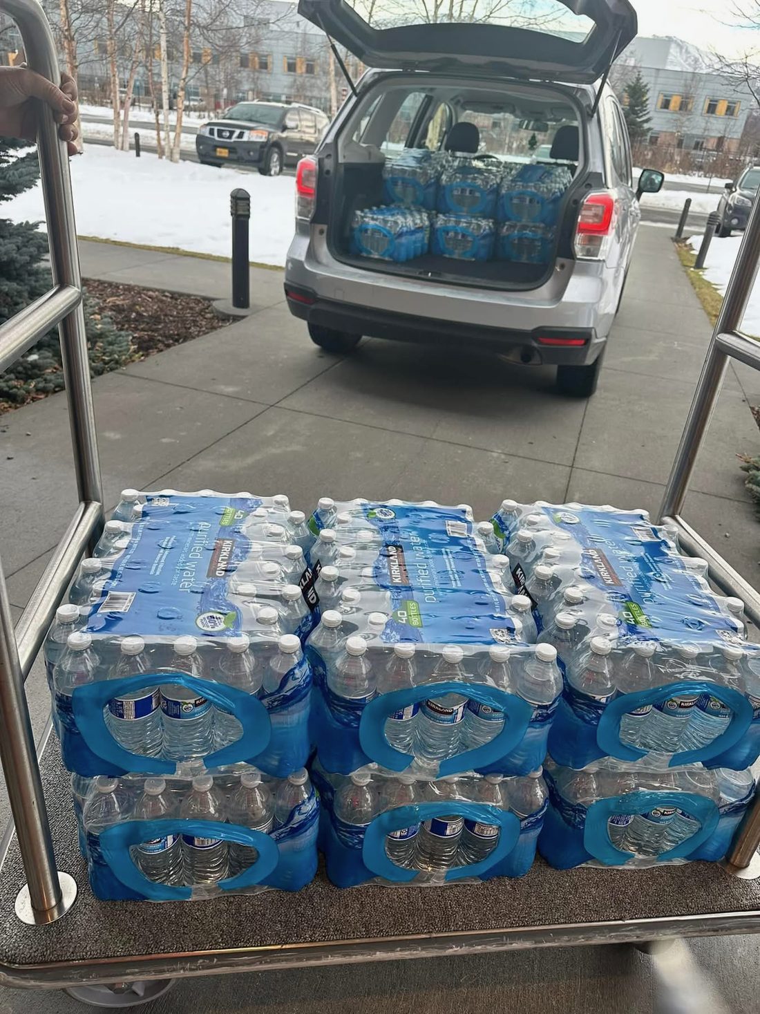 Cases of bottled water on a cart being unloaded from a car outside the house
