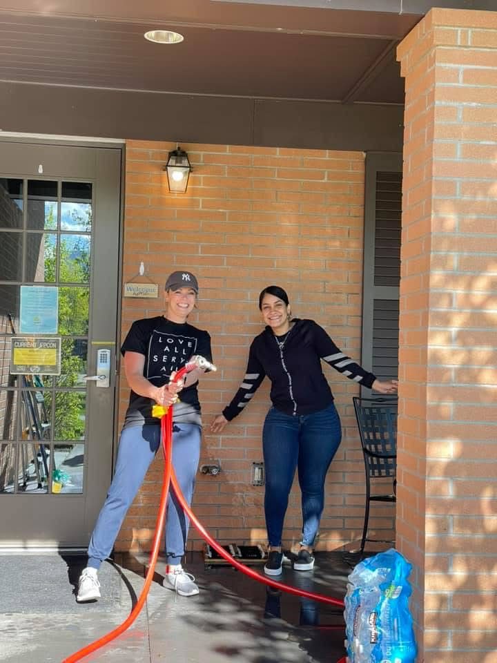 Two volunteers with a garden hose on the Fisher House porch